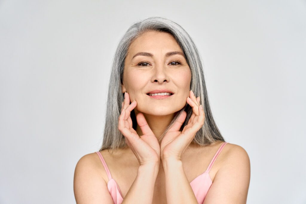 Confident mature woman with long gray hair smiling and touching her face